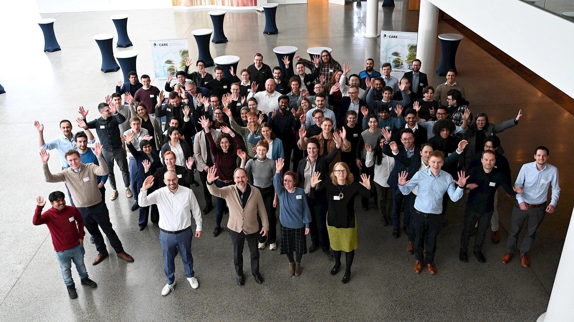 A group photo taken from above, with the participants waving at the camera.