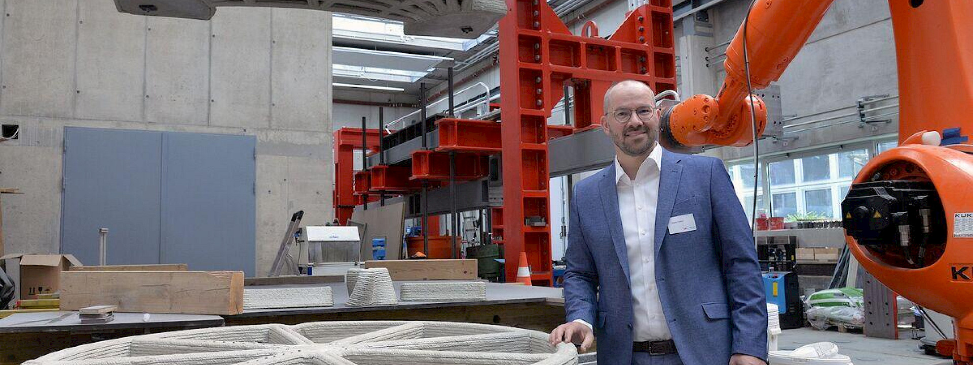 A person in a laboratory in front of a industrial robot and a concrete 3d-printed component