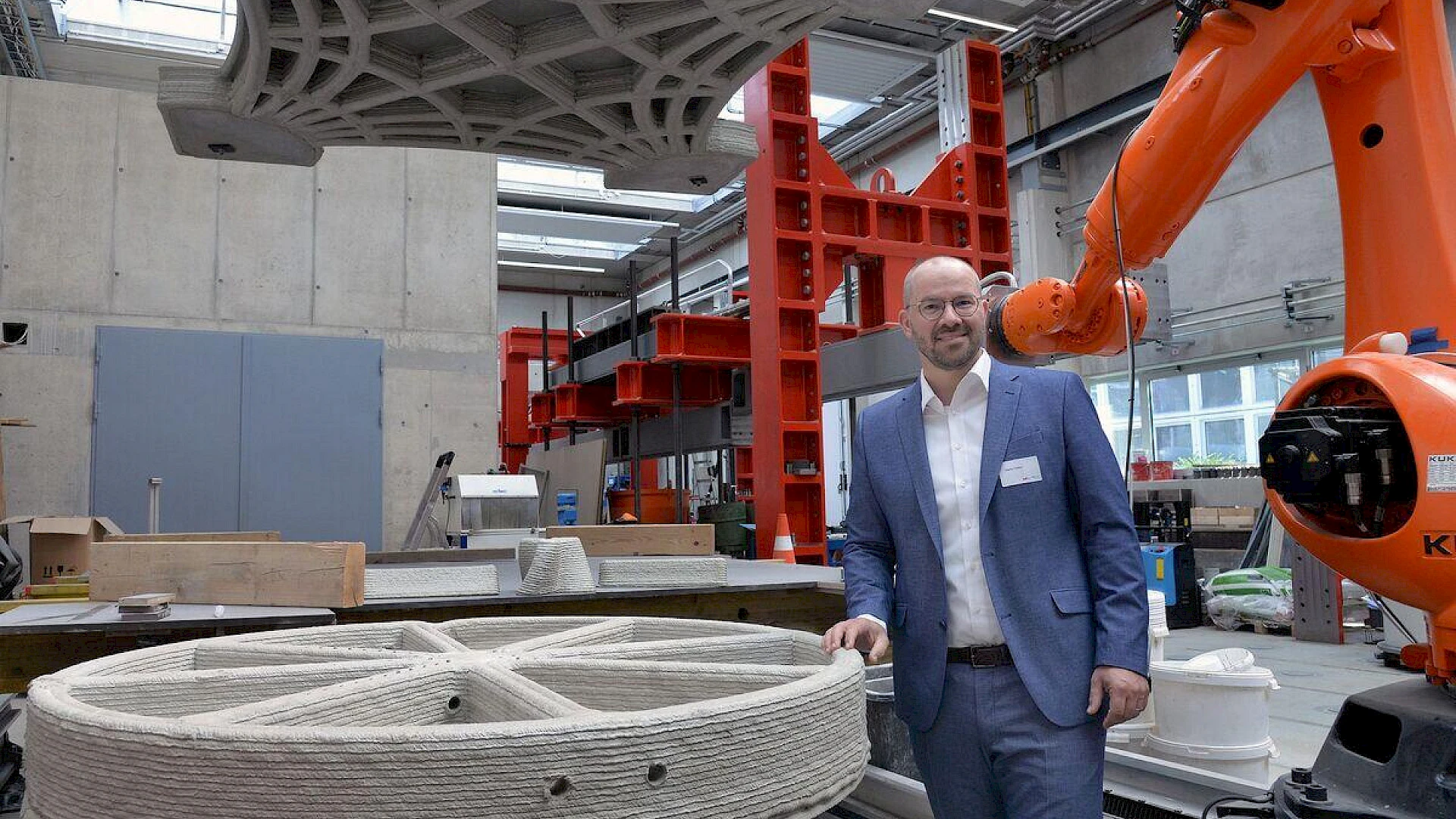 A person in a laboratory in front of a industrial robot and a concrete 3d-printed component