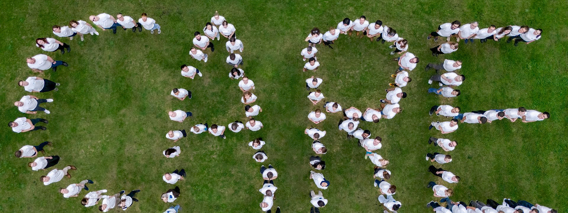 a group of people on a lawn forming the letters "CARE" with their bodies