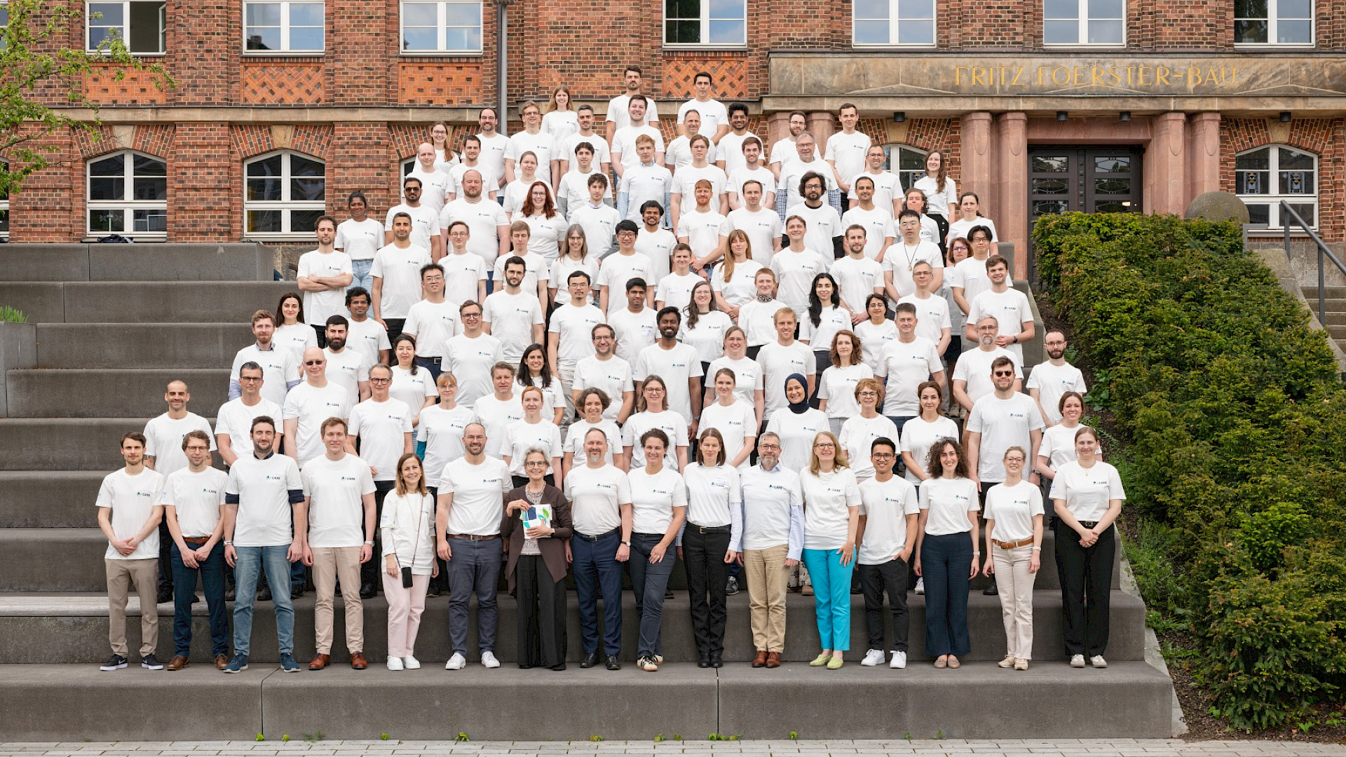 A group photo of people, all with the same white t-shirt on a big staircase in front of a brick building